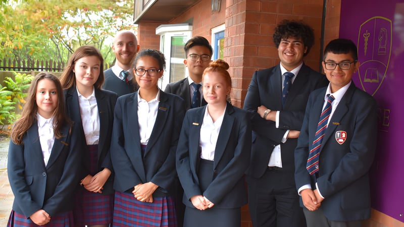 Eine Gruppe Schülerinnen und Schüler der Chase Grammar School steht gemeinsam vor einem Backsteingebäude mit Pflanzen im Hintergrund.