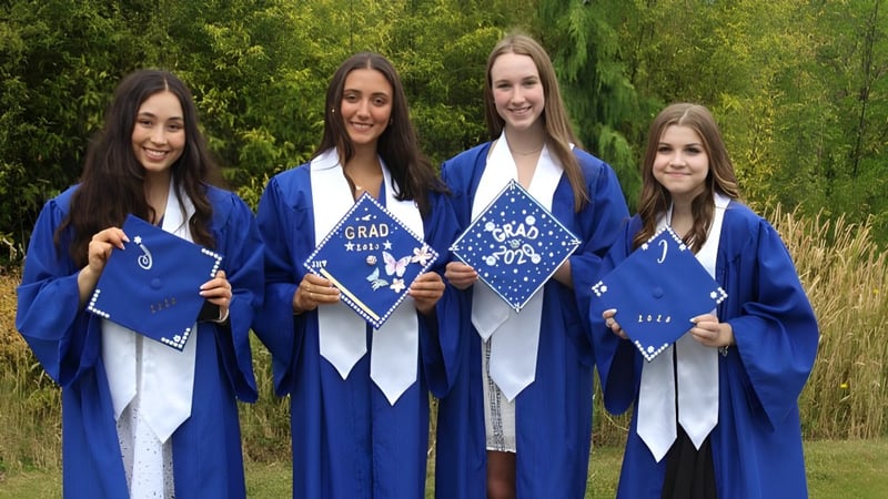 Vier Schülerinnen in blauen Abschlussroben stehen gemeinsam im Grünen auf dem Gelände der Chatelech Secondary School.