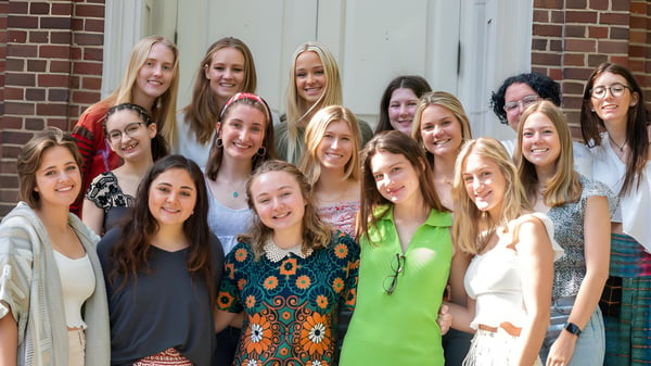Eine Gruppe junger Schülerinnen steht lächelnd vor einem Backsteingebäude auf dem Campus der Chatham Hall School.