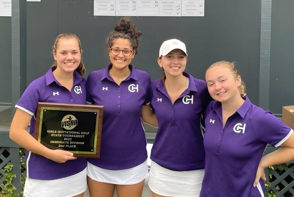 Vier Schuelerinnen der Chatham Hall School in violetten Uniformen halten eine Trophaee vor einem Gebaeude.