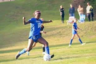Eine Fußballspielerin der Chapel Hill - Chauncy Hall dribbelt den Ball auf dem Spielfeld mit weiteren Spielern im Hintergrund.