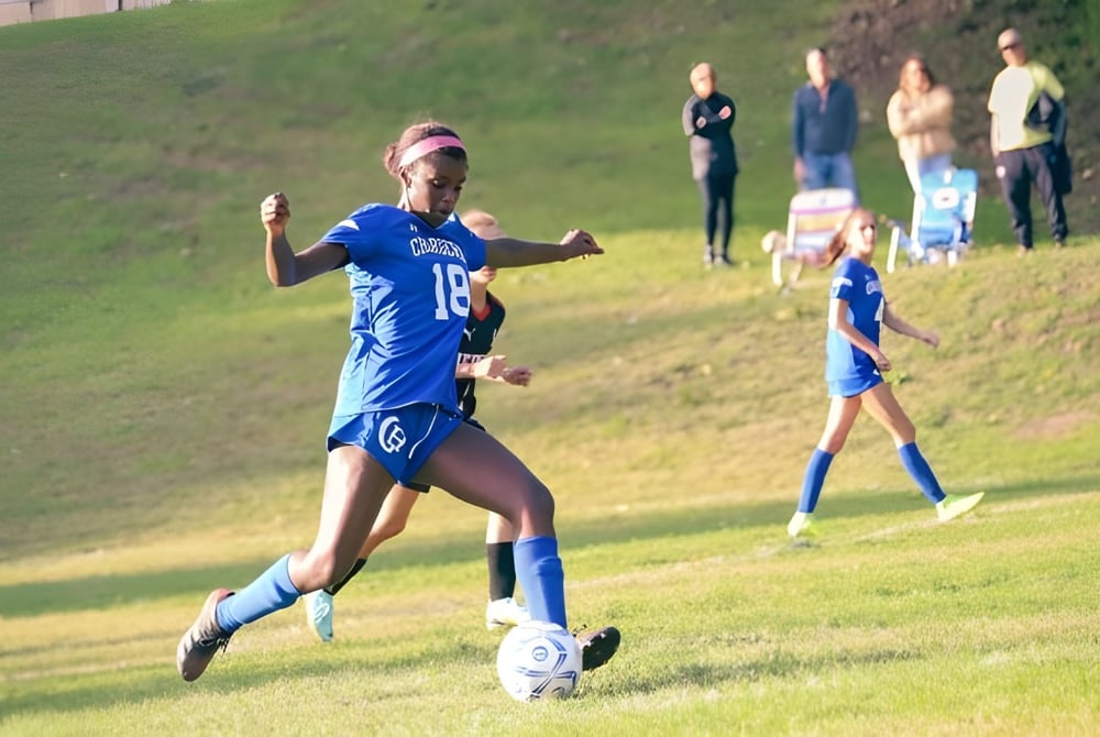 Eine Fußballspielerin der Chapel Hill - Chauncy Hall dribbelt den Ball auf dem Spielfeld mit weiteren Spielern im Hintergrund.