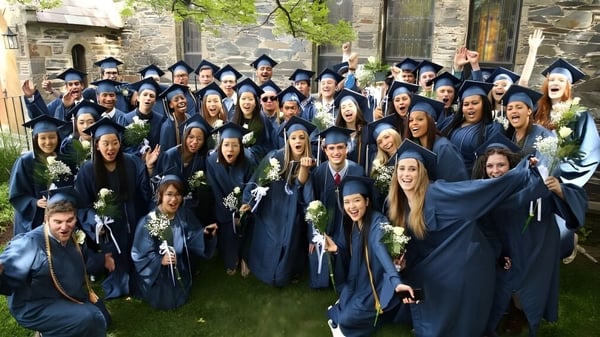 Absolventinnen und Absolventen von Chapel Hill - Chauncy Hall stehen in blauen Abschlussroben im Freien vor einem steinernen Gebäude.