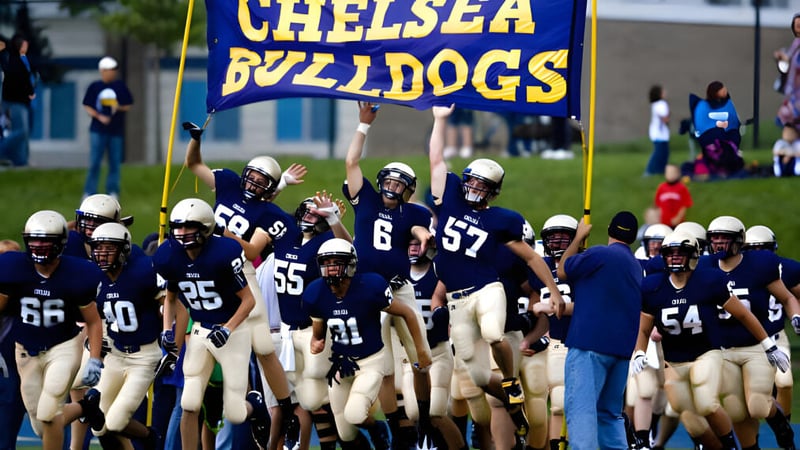 Schüler der Chelsea High School stehen in Fußballuniformen auf dem Spielfeld mit Zuschauern im Hintergrund.