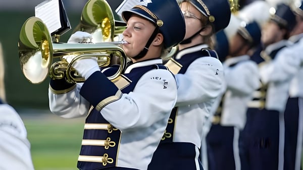 Ein Mitglied der Marching Band der Chelsea High School spielt ein Blechblasinstrument in weiß-blauem Uniform.
