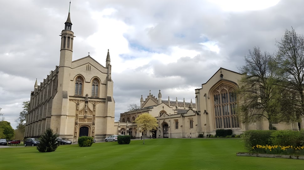Eine prächtige gotische Kathedrale mit hohem Turm steht im grünen Innenhof des Cheltenham College unter bewölktem Himmel.