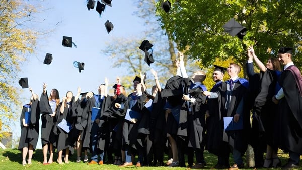 Absolventen des Cheltenham College werfen ihre Abschlussmützen in die Luft vor grünen Bäumen.