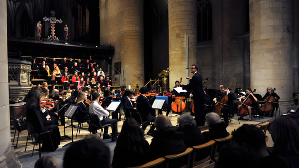 Das Orchester der Cheltenham College spielt auf einer Bühne in einer großen Kathedrale vor einem Publikum.