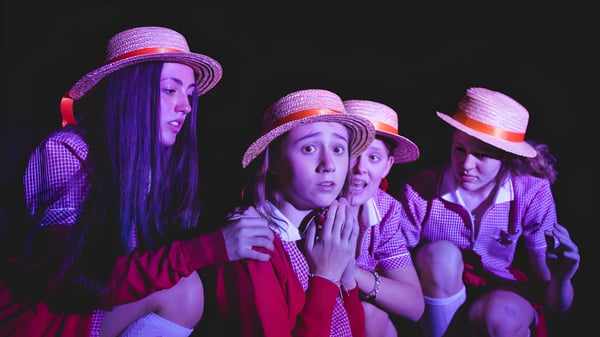 Eine Gruppe von Schülerinnen der Cheltenham Ladies' College trägt bunte Kleidung und Hüte in einer dunklen Umgebung.