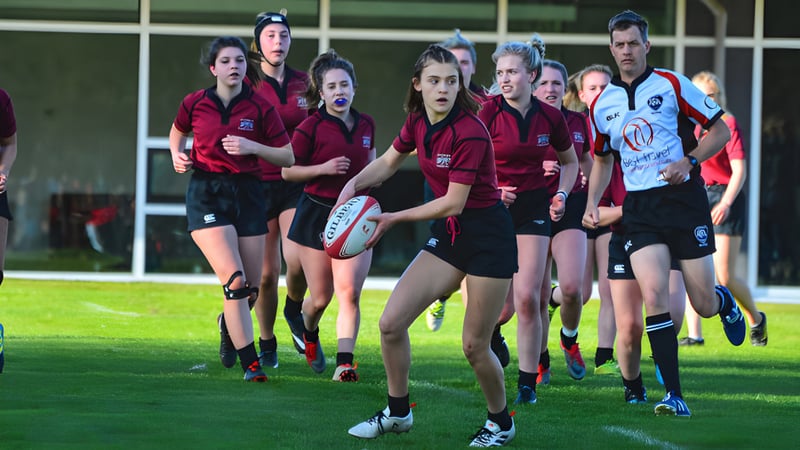 Eine Gruppe von Rugby-Spielerinnen der Chemainus Secondary School steht auf einem Rasenfeld mit einer gegnerischen Mannschaft im Hintergrund.