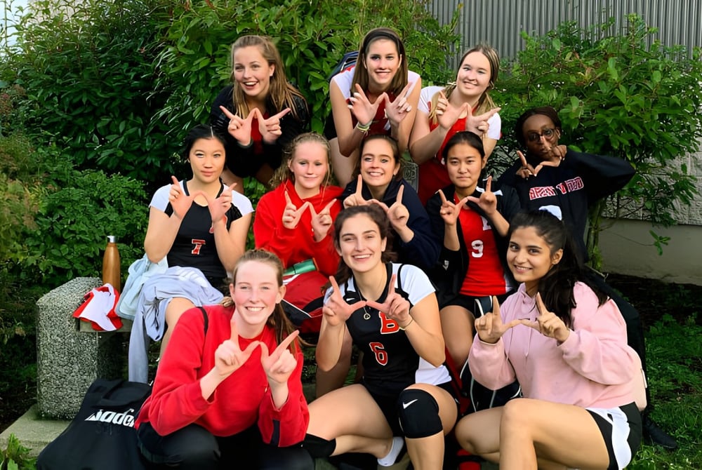 Eine Gruppe Schülerinnen der Chemainus Secondary School steht im Freien in Sportbekleidung und macht Handgesten vor grüner Kulisse.