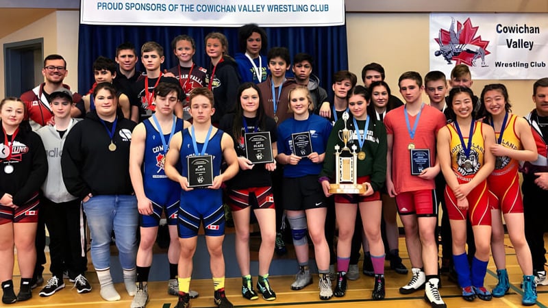 Eine Gruppe junger weiblicher Ringerinnen der Chemainus Secondary School steht mit Pokalen vor einem Banner des Cowichan Valley Wrestling Club.