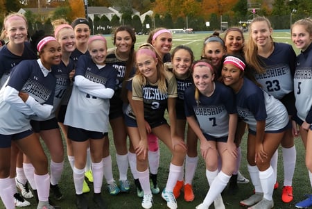 Eine Gruppe junger Athletinnen der Cheshire Academy steht im Freien vor herbstlicher Kulisse und lacht zusammen.