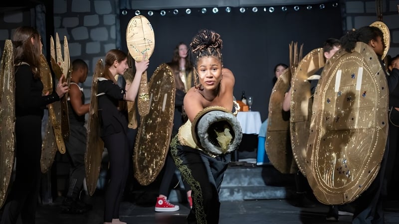 Eine Schülerin der Cheshire Academy trägt ein goldenes Kostüm bei einem Bühnenauftritt mit anderen Darstellern.