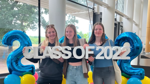 Drei Schülerinnen halten vor einem Gebäude auf dem Campus der Cheshire College South & West ein großes Schild mit CLASS OF 2022.