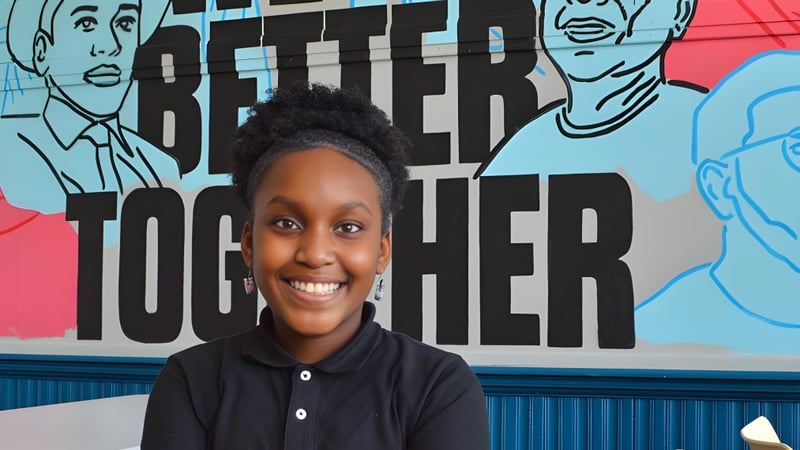 Ein Jugendlicher steht vor einem bunten Wandbild mit der Aufschrift ‚Better Together‘ auf dem Gelände der Chicago Public Schools.