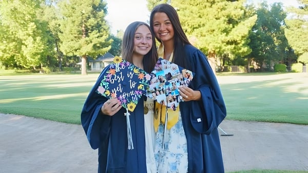 Zwei Schülerinnen in farbenfrohen Abschlussroben stehen im Park des Chico Unified School District und lächeln zusammen.