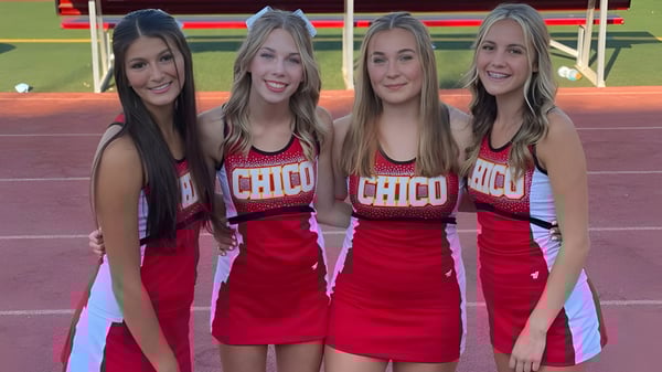 Vier Schülerinnen in roten Cheerleading-Uniformen stehen auf dem Sportfeld des Chico Unified School District.