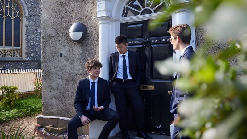 Schüler und Mitarbeiter der Chigwell School in formeller Kleidung stehen vor einem Gebäude mit historischer Architektur.