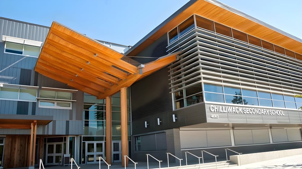 Das moderne mehrstöckige Gebäude der Chilliwack Secondary School mit orange-grauer Fassade und großen Glasfenstern bei blauem Himmel.
