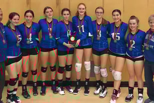 Eine Gruppe junger Volleyballspielerinnen der Chilliwack Secondary School steht gemeinsam vor einem Holzhintergrund.