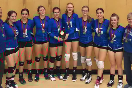 Eine Gruppe junger Volleyballspielerinnen der Chilliwack Secondary School steht gemeinsam vor einem Holzhintergrund.