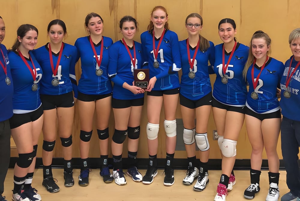Eine Gruppe junger Volleyballspielerinnen der Chilliwack Secondary School steht gemeinsam vor einem Holzhintergrund.