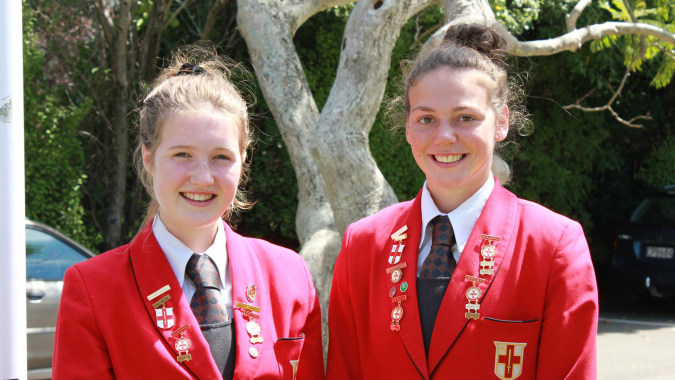 Zwei Schülerinnen der Chilton Saint James School stehen lächelnd vor einem bewaldeten Hintergrund.