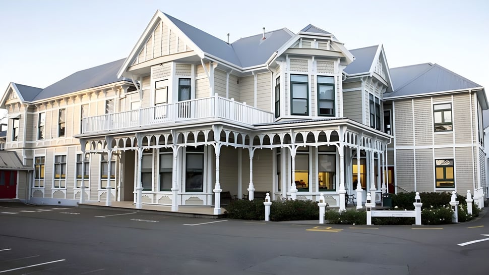 Das viktorianische Hauptgebäude der Chilton Saint James School mit einer umlaufenden Veranda ist von einer Straße und geparkten Autos umgeben.
