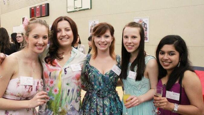 Eine Gruppe von Schülerinnen der Chilton Saint James School posiert zusammen in farbenfrohen Kleidern vor einem Basketballkorb.
