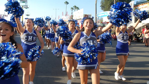 Cheerleader in blauen und weißen Uniformen marschieren mit Pompons entlang einer von Palmen gesäumten Straße beim Chino Valley Unified School District.