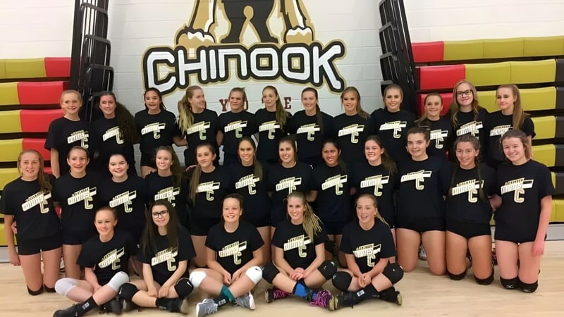 Eine Gruppe junger Athletinnen der Chinook High School posiert in der Sporthalle vor Matten und Geräten.
