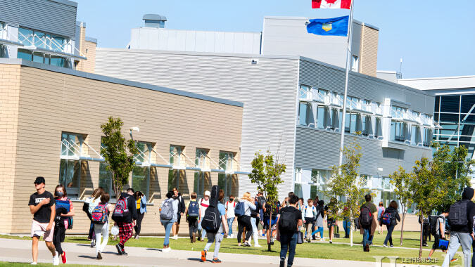 Eine Gruppe von Schülerinnen und Schülern geht über den grasbewachsenen Campus der Chinook High School mit kanadischer Flagge und modernen Gebäuden im Hintergrund.