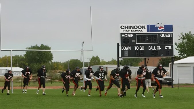 Schüler der Chinook High School stehen in Fußballuniform auf dem Sportfeld vor der Anzeigetafel.