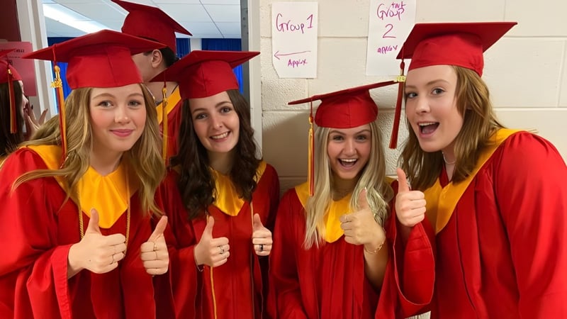 Vier Schülerinnen der Chippewa Secondary School in roten Abschlussroben und Hüten zeigen im Klassenraum Daumen nach oben.