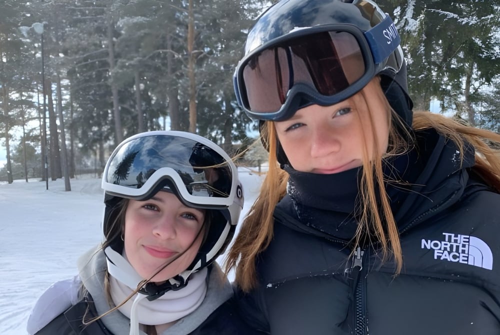 Zwei Personen mit Winterausrüstung stehen in einem verschneiten Wald auf dem Gelände der Chippewa Secondary School.