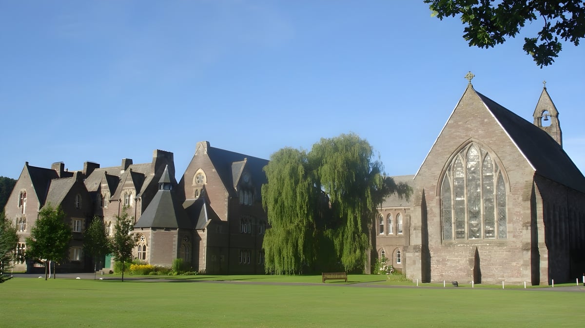 Der Campus von Christ College zeigt einen gepflegten grünen Rasen und mehrere historische Gebäude im gotischen Stil unter klarem Himmel.