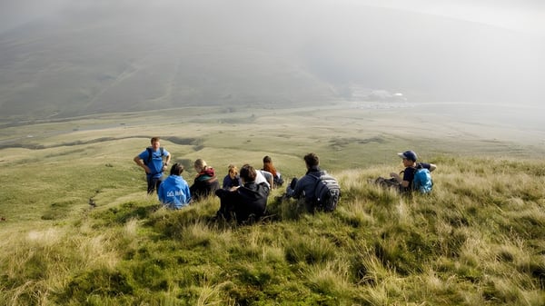 Eine Gruppe Schüler des Christ College steht auf einer Wiese vor nebligen Bergen.