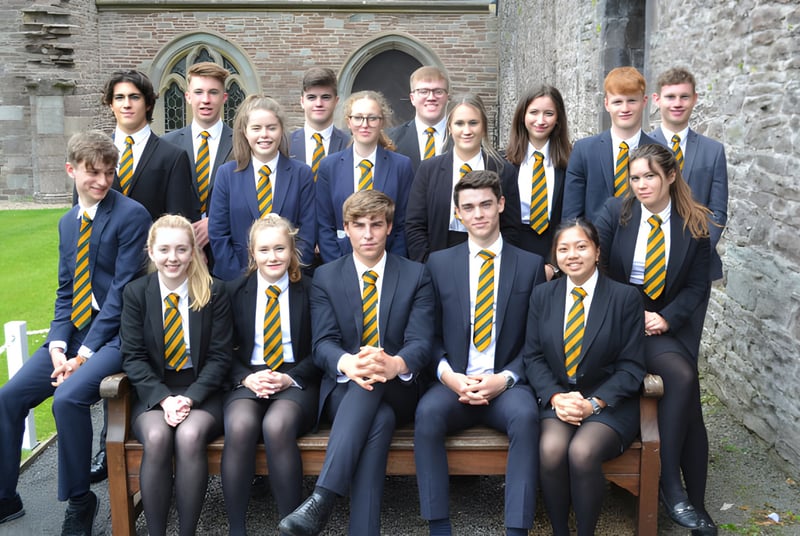 Eine Gruppe Schüler in Uniform steht vor dem historischen Steingebäude des Christ College und posiert für ein Foto.