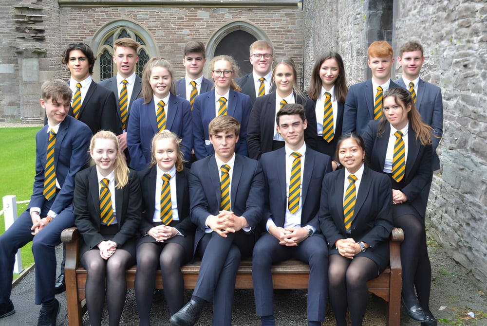 Eine Gruppe Schüler in Uniform steht vor dem historischen Steingebäude des Christ College und posiert für ein Foto.
