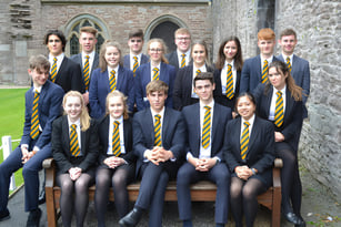 Eine Gruppe Schüler in Schuluniformen posiert vor einem historischen Steinbau auf dem Campus des Christ College.