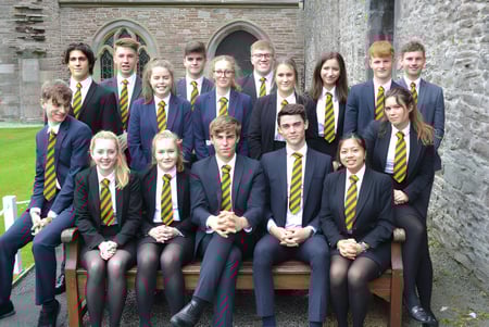 Eine Gruppe Schüler in Schuluniformen posiert vor einem historischen Steinbau auf dem Campus des Christ College.