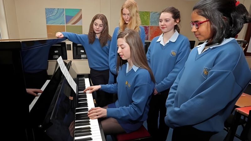 Schüler der Christ King Secondary School in blauen Uniformen spielen gemeinsam Klavier vor bunten Kunstwerken.