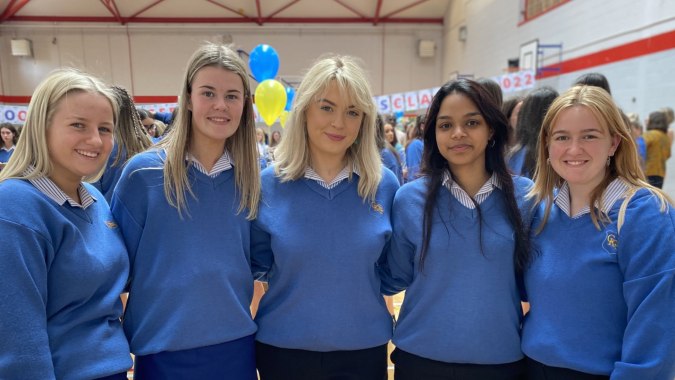 Fünf Schülerinnen der Christ King Secondary School stehen in blauen Schuluniformen im Schulflur mit bunten Dekorationen im Hintergrund.