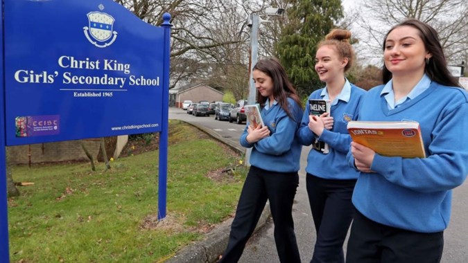 Drei Schülerinnen stehen vor dem Schild der Christ King Secondary School und führen eine Unterhaltung.