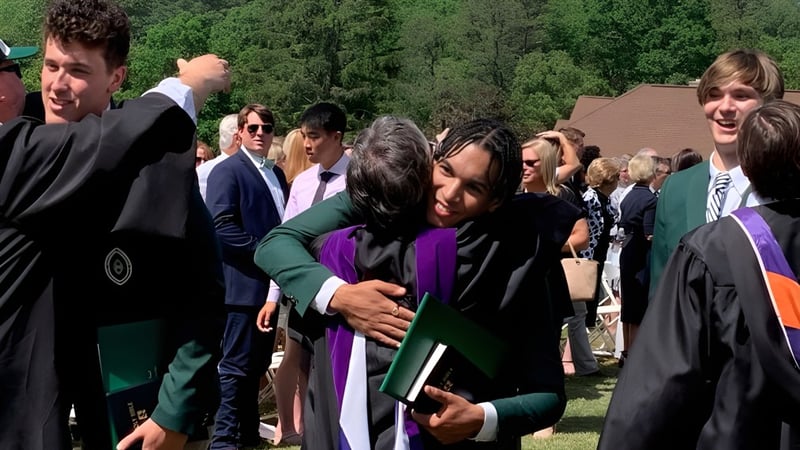 Eine Gruppe von Absolventinnen und Absolventen in Talaren versammelt sich im Freien auf dem Campus der Christ School.