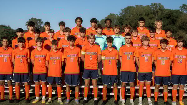 Eine Gruppe junger Fußballspielerinnen und Fußballspieler der Christchurch School steht gemeinsam auf einem Feld mit Bäumen und blauem Himmel.