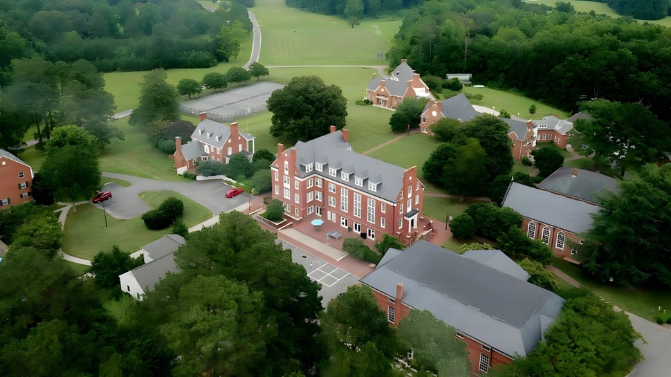 Luftaufnahme des historischen Backsteingebäudes der Christchurch School umgeben von grüner Landschaft und einer Landstraße.