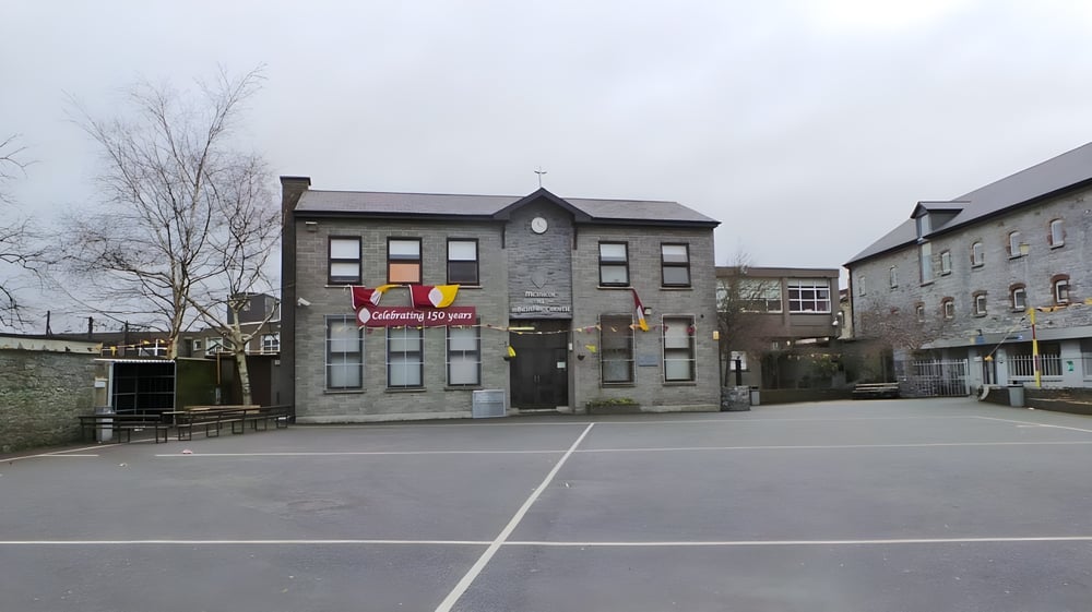 Das steinerne Hauptgebäude der Christian Brothers School Kilkenny mit mehreren Fenstern und einem gepflasterten Hof im Vordergrund.
