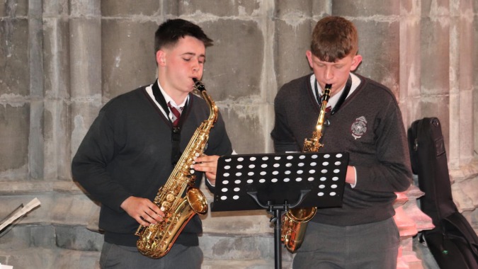 Zwei Schüler der Christian Brothers School Kilkenny spielen vor einer Betonwand Musik, einer mit Saxophon, der andere mit Notenständer.